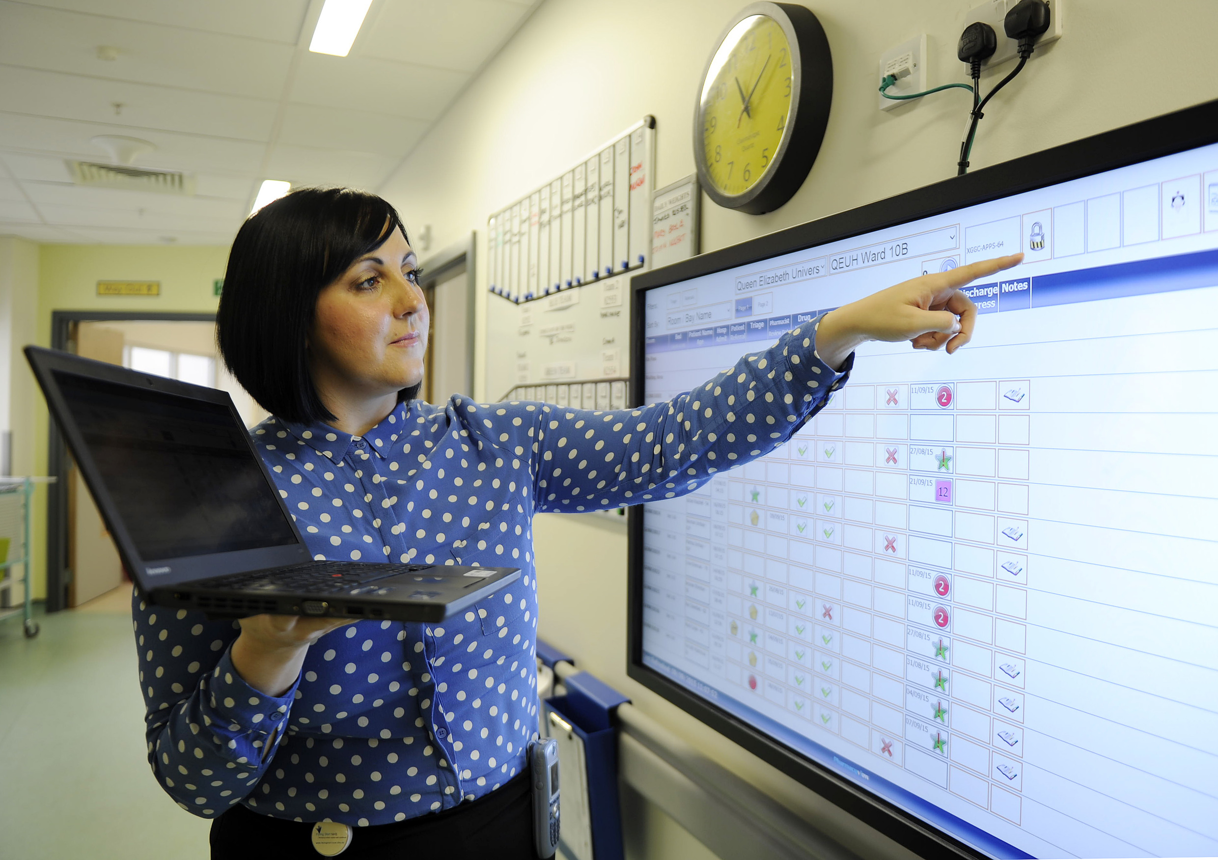 Woman checking computer against board in hospital